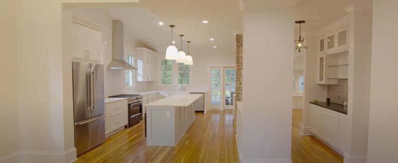 After: finished open kitchen with white cabinets, an island, pendant lights and wood floors