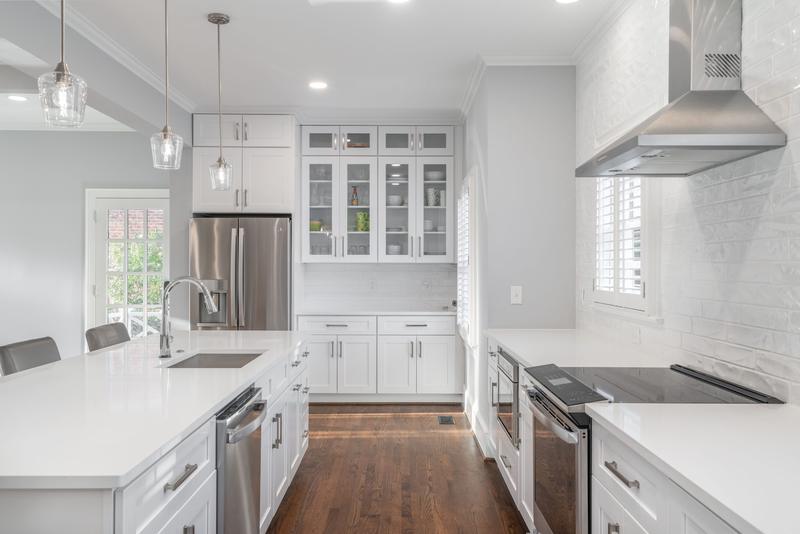 White kitchen with glass-front upper cabinets and a stainless chimney hood
