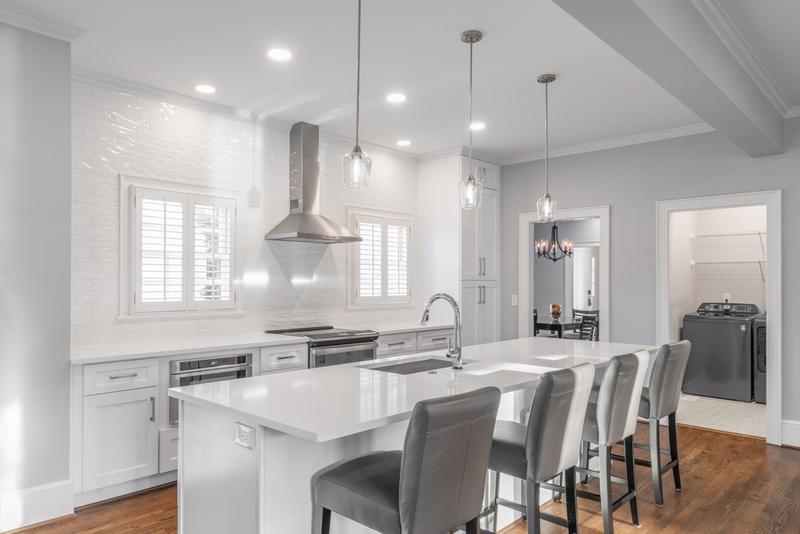 White kitchen island with gray bar stools and glass pendant lights