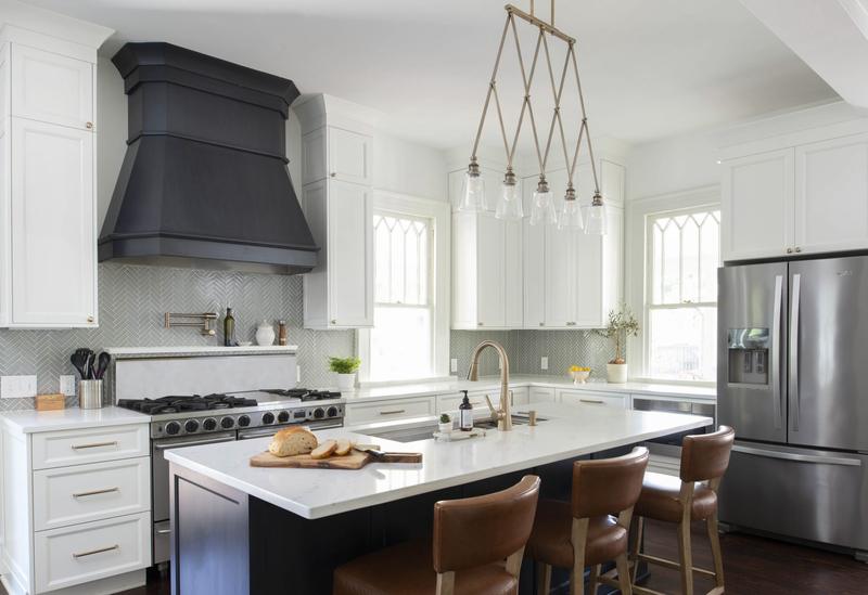 Remodeled white kitchen with a black range hood, marble island and pendant lights