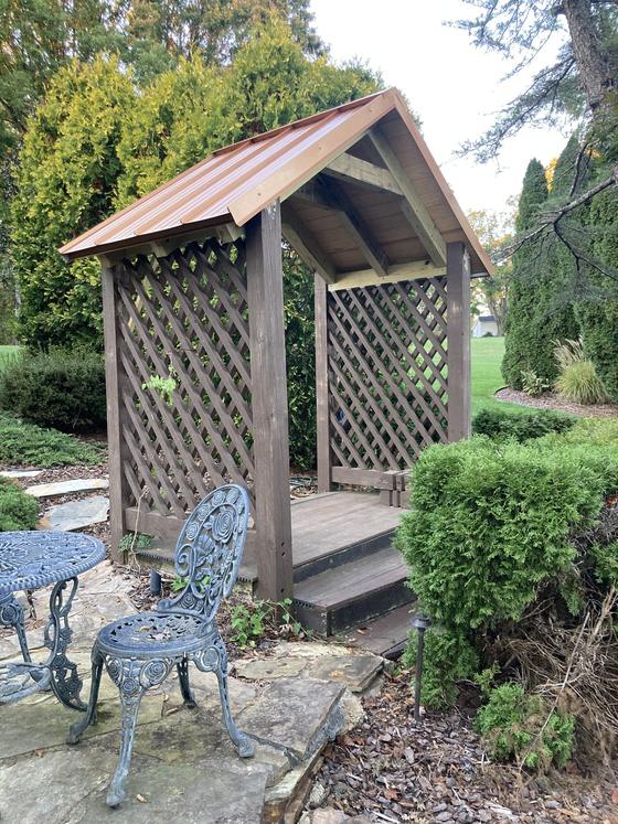 Wood arbor with a copper roof over a stone garden patio